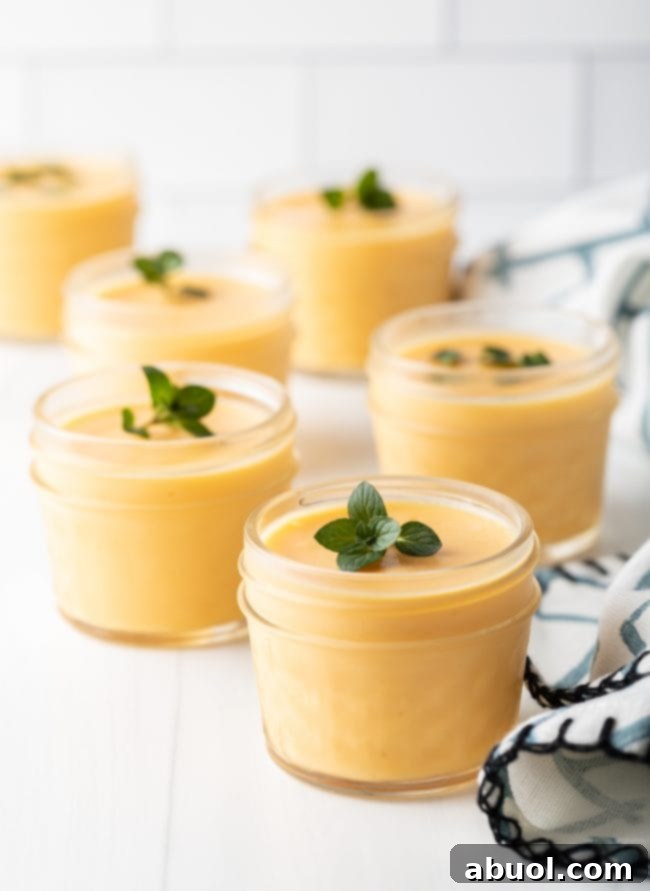 A row of individual glass cups filled with dairy-free mango pudding, each beautifully garnished with a mint leaf, ready to be served.