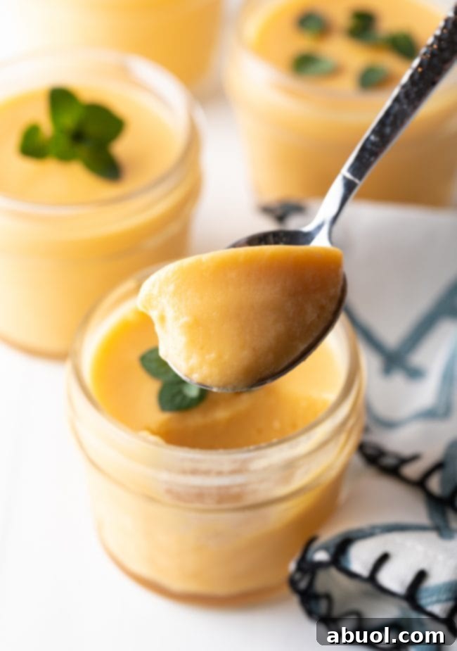 A spoon digging into a cup of rich, creamy dairy-free mango pudding, showcasing its smooth texture and vibrant color.