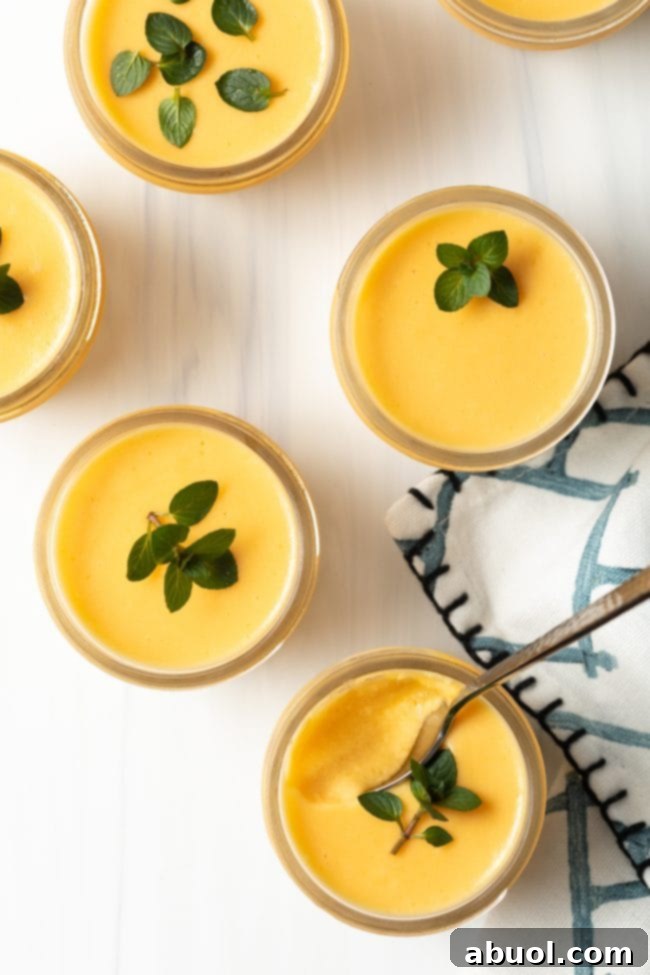 Overhead view of four elegant glass cups filled with creamy dairy-free mango pudding, each topped with a fresh mint leaf.