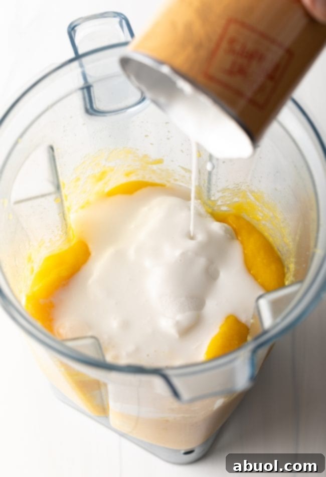 Step 4: Adding coconut milk and vanilla extract to the mango puree in the blender.