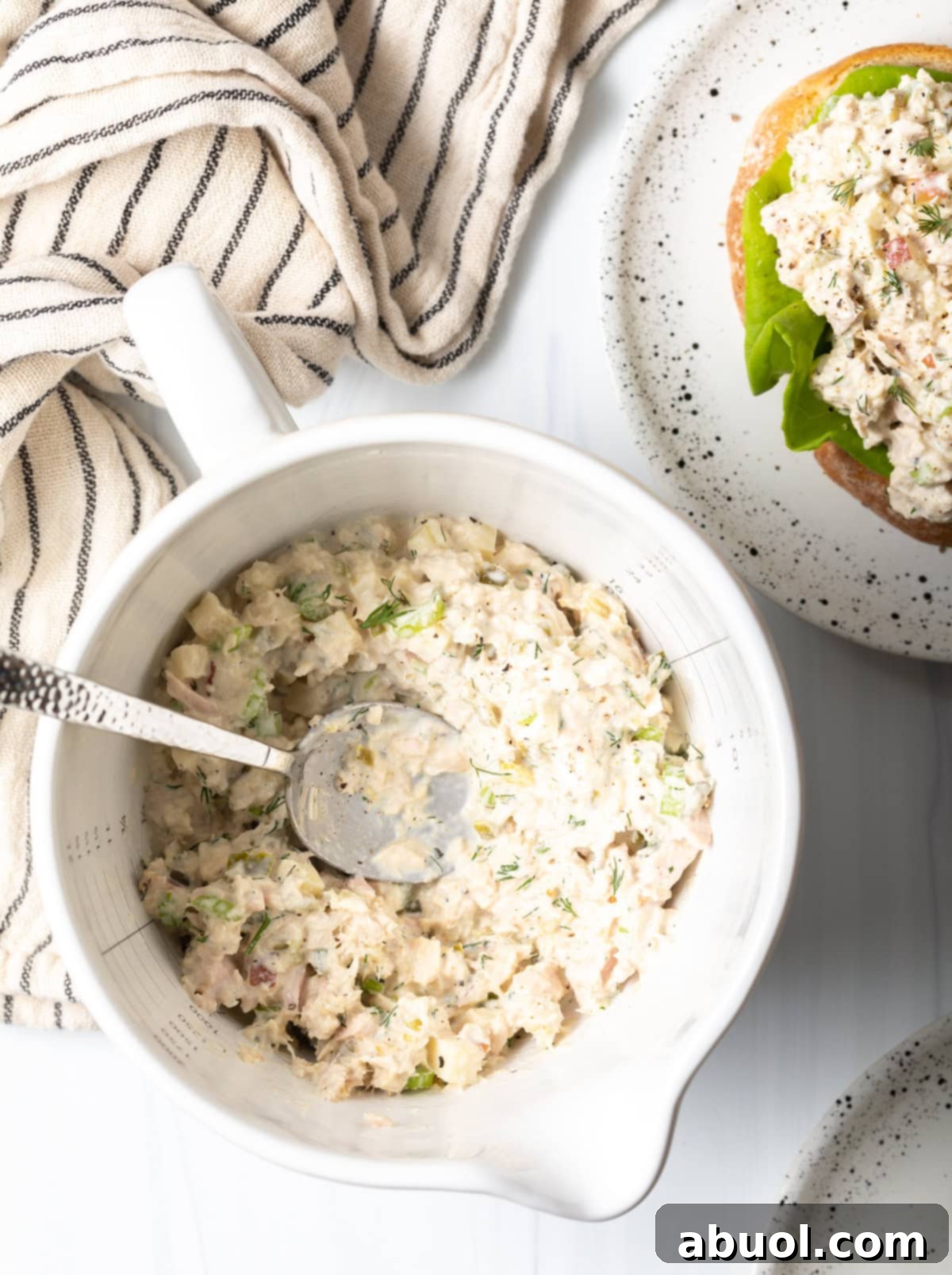 A vibrant white bowl of unique tuna salad with crisp apple pieces, captured from an overhead perspective, with a spoon resting beside it.