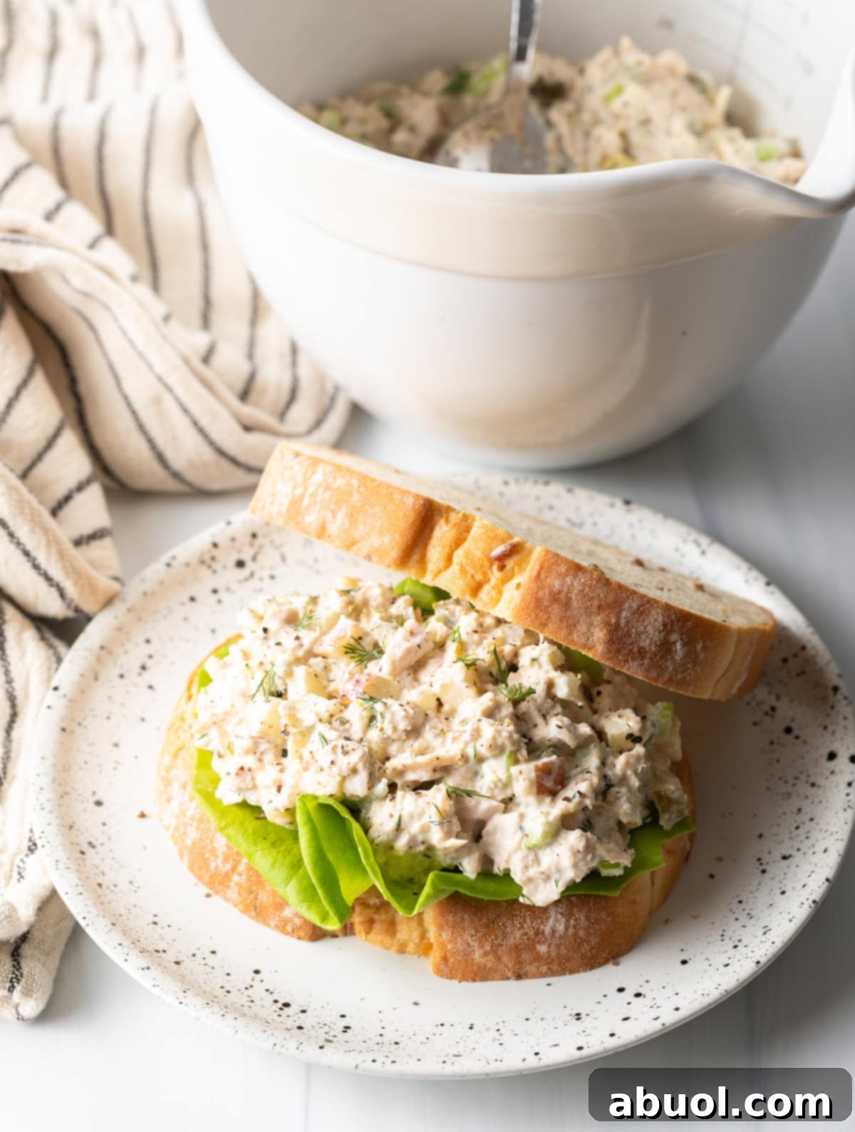A side view of a beautifully presented bowl of tuna salad, accompanied by a homemade tuna sandwich and a fresh side salad on a white plate.