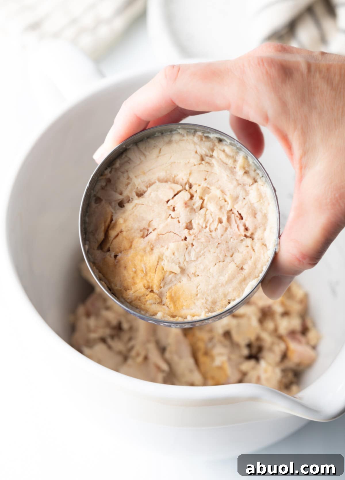 A hand holding a can of tuna in water, ready to be drained for the recipe.