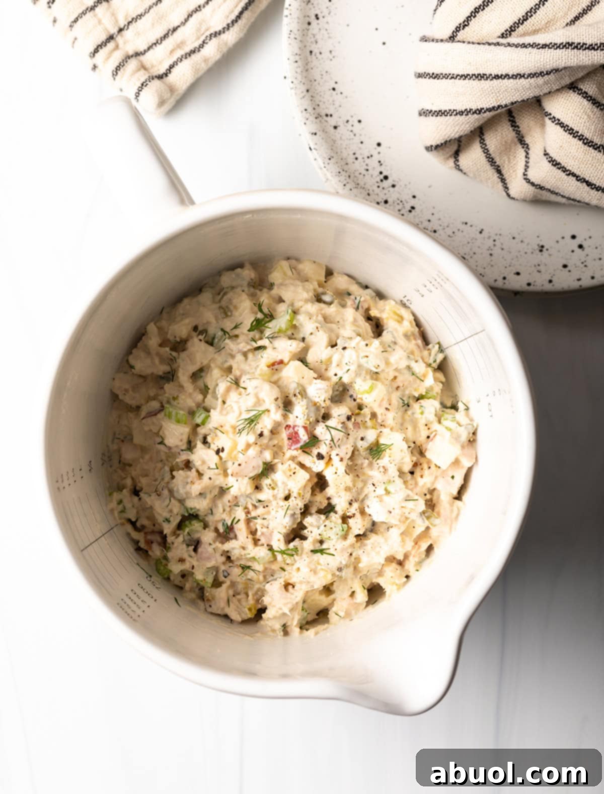 An inviting overhead view of a bowl of homemade classic tuna salad, studded with apple pieces and fresh dill.