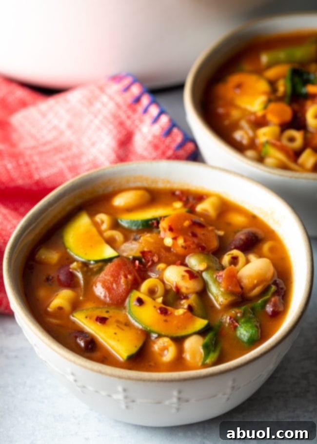 Close-up view of Olive Garden Minestrone Soup, showcasing vibrant tomatoes, zucchini, beans, ditalini pasta, and fresh spinach.