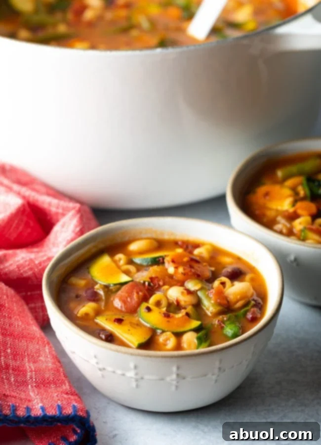 Two steaming bowls of Olive Garden Minestrone Soup, rich with pasta and vegetables, positioned in front of a larger pot of soup.