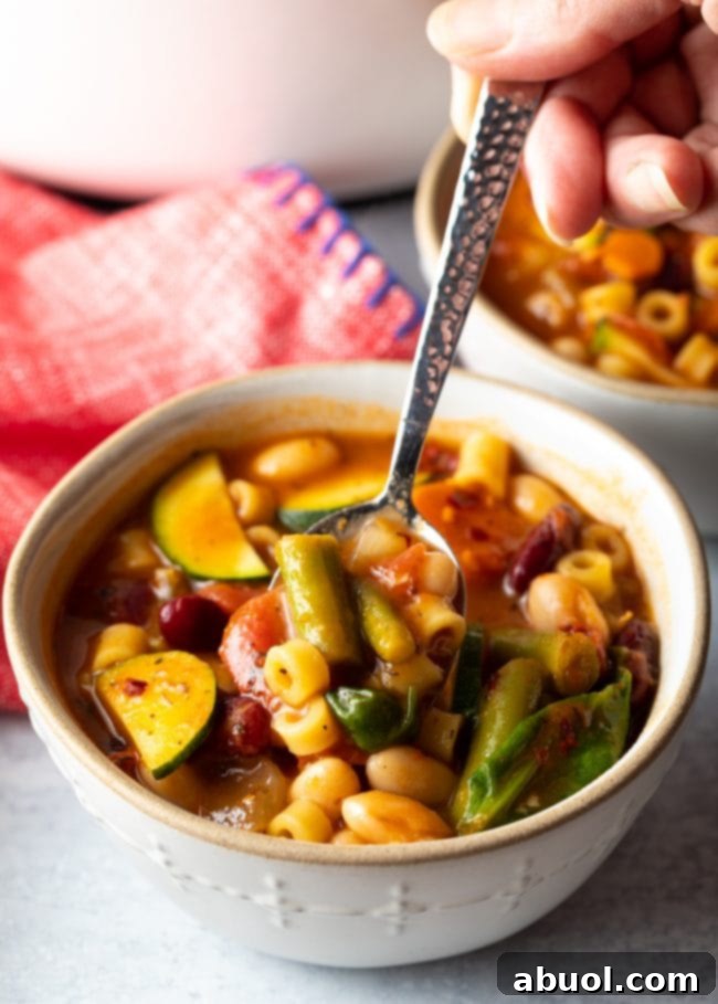 A spoon scooping a generous portion of copycat Olive Garden Minestrone Soup, showcasing a rich blend of pasta, beans, and fresh vegetables.