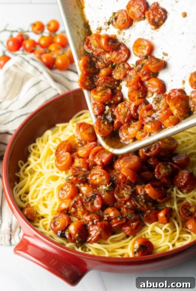 Pouring the roasted tomatoes from the baking sheet onto a bed of pasta.