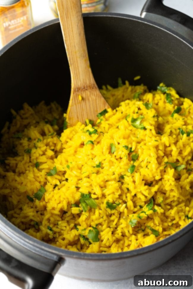 A wooden spoon mixes the yellow rice with cilantro. 
