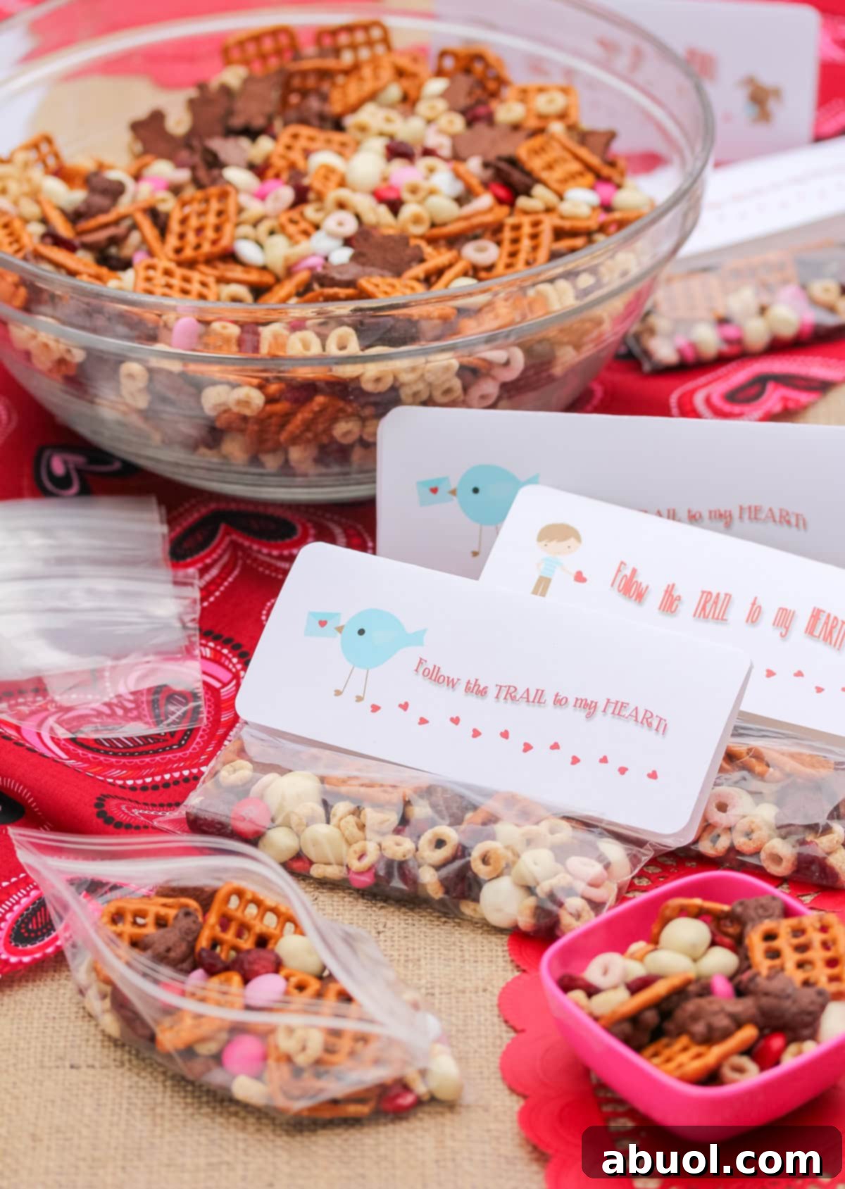 A vibrant Valentine's Day Trail Mix, perfectly portioned into individual baggies, with a large bowl of the mix visible in the background. The scene suggests a festive, shareable treat.