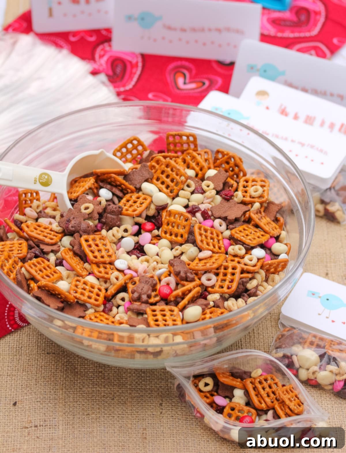 A close-up view of homemade Valentine's Day trail mix in a large mixing bowl, with neatly arranged individual gift bags and printable tags nearby, emphasizing the DIY aspect.