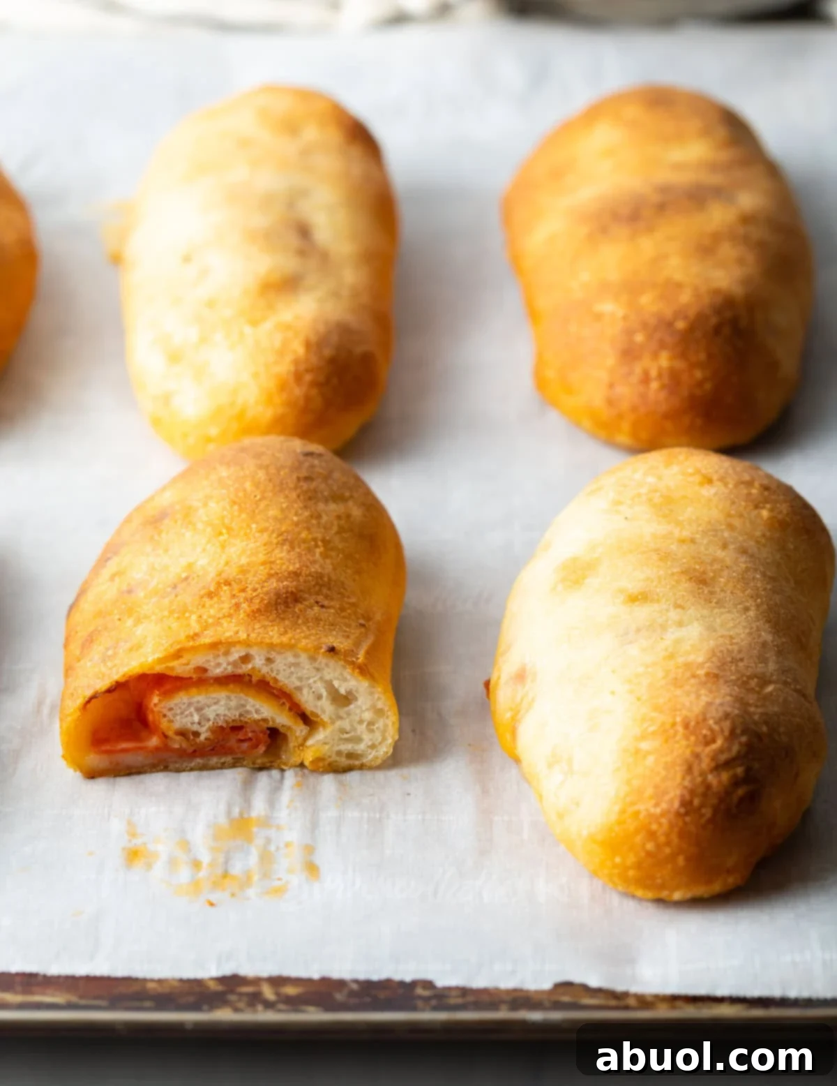 side view of sliced open pepperoni roll on a baking sheet with whole loaves