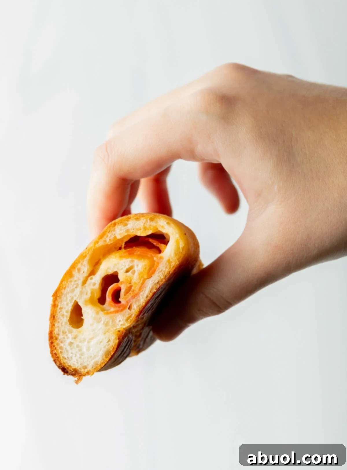 hand holding half of a pizza roll with cheese and meat