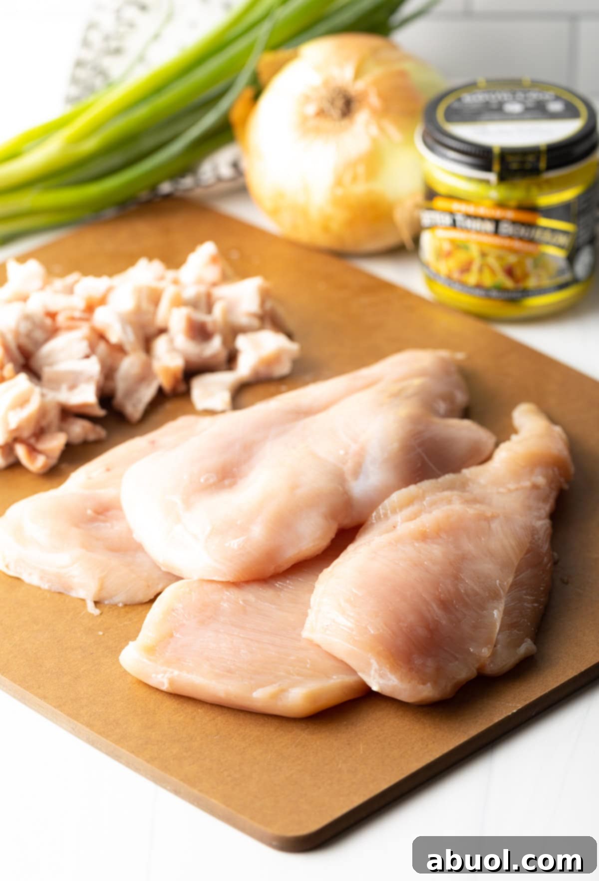 A selection of fresh ingredients for Smothered Chicken laid out on a cutting board and counter, including raw chicken breasts, chopped bacon, onion, flour, and various seasonings, ready for preparation.