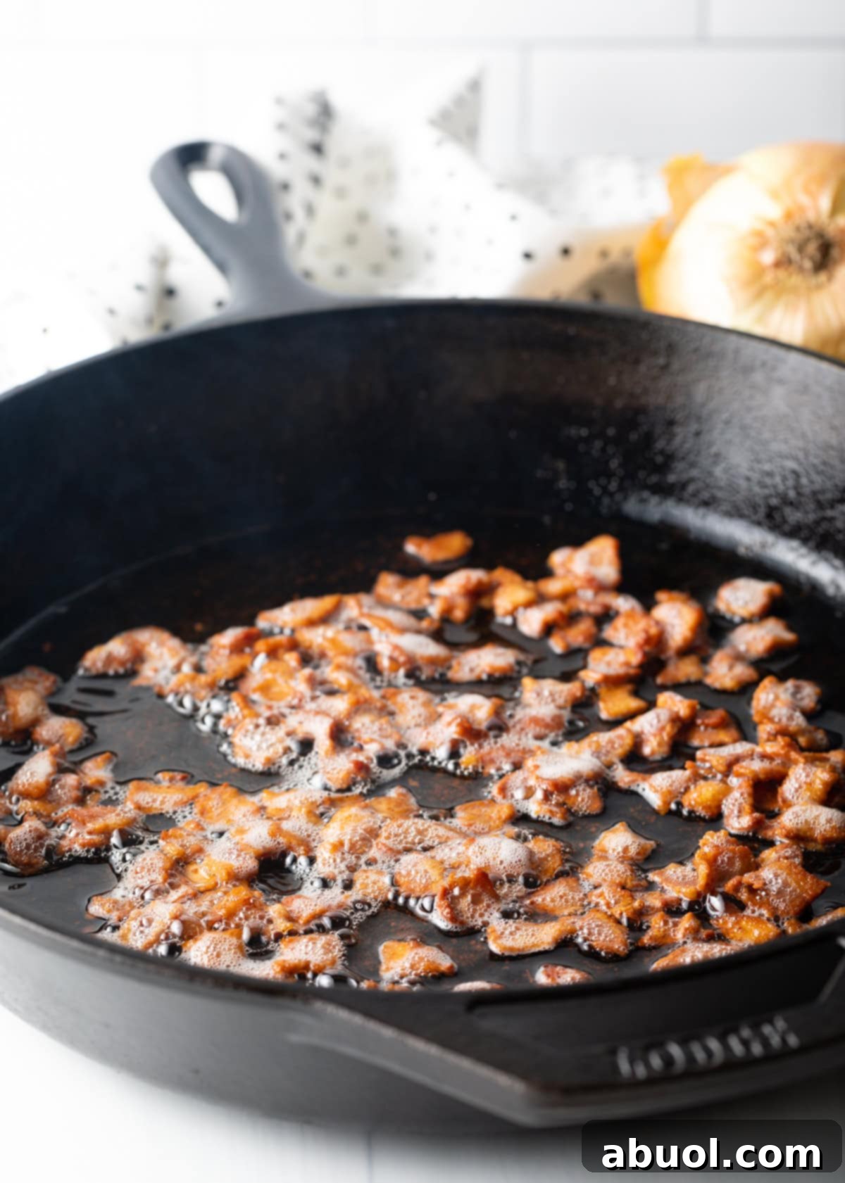 Close-up view of chopped bacon sizzling and cooking in a cast iron skillet, rendering its fat and becoming crispy.