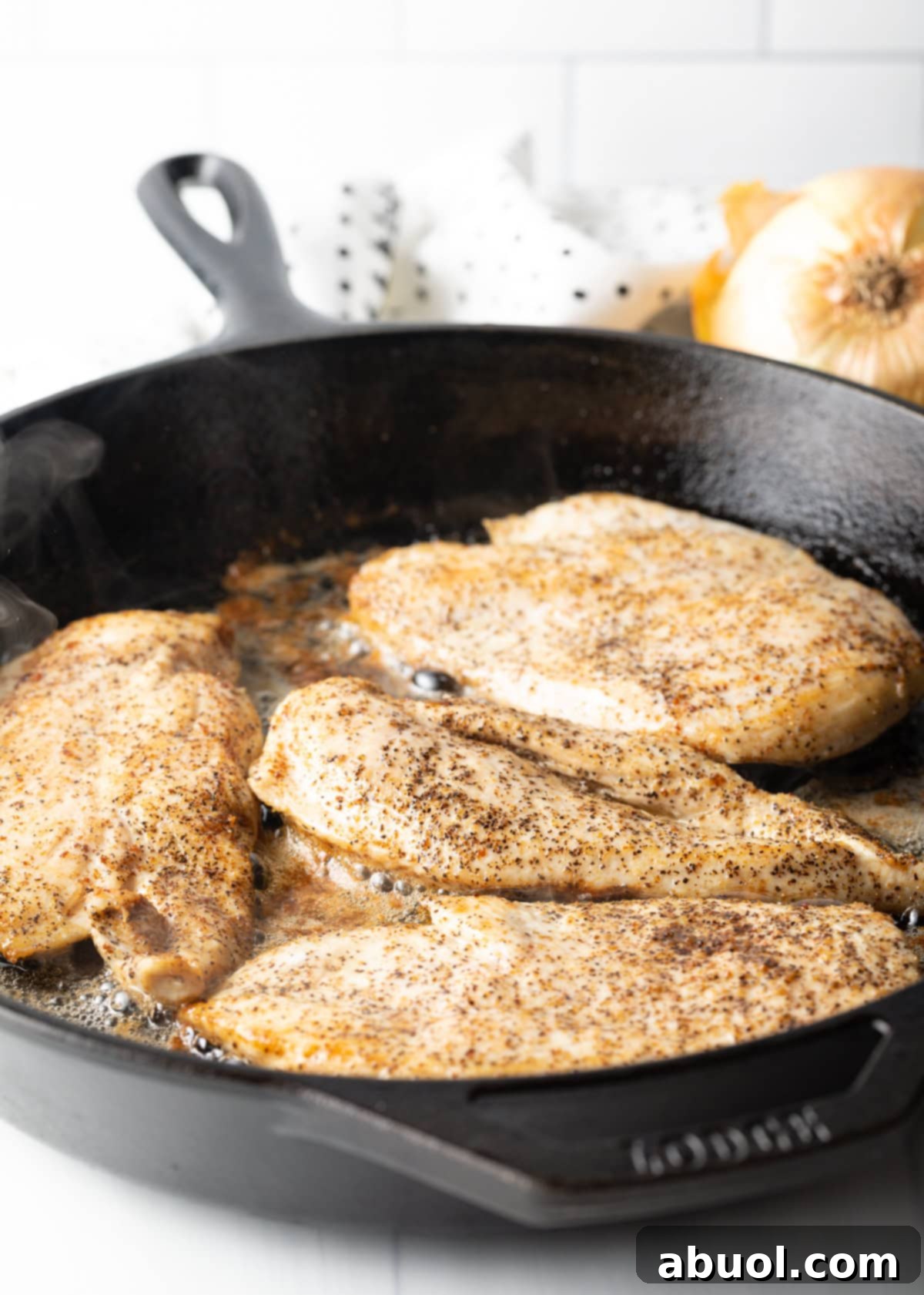 Seasoned chicken breasts browning in hot bacon grease within a cast iron skillet, showing the beginning stages of cooking for the smothered chicken recipe.