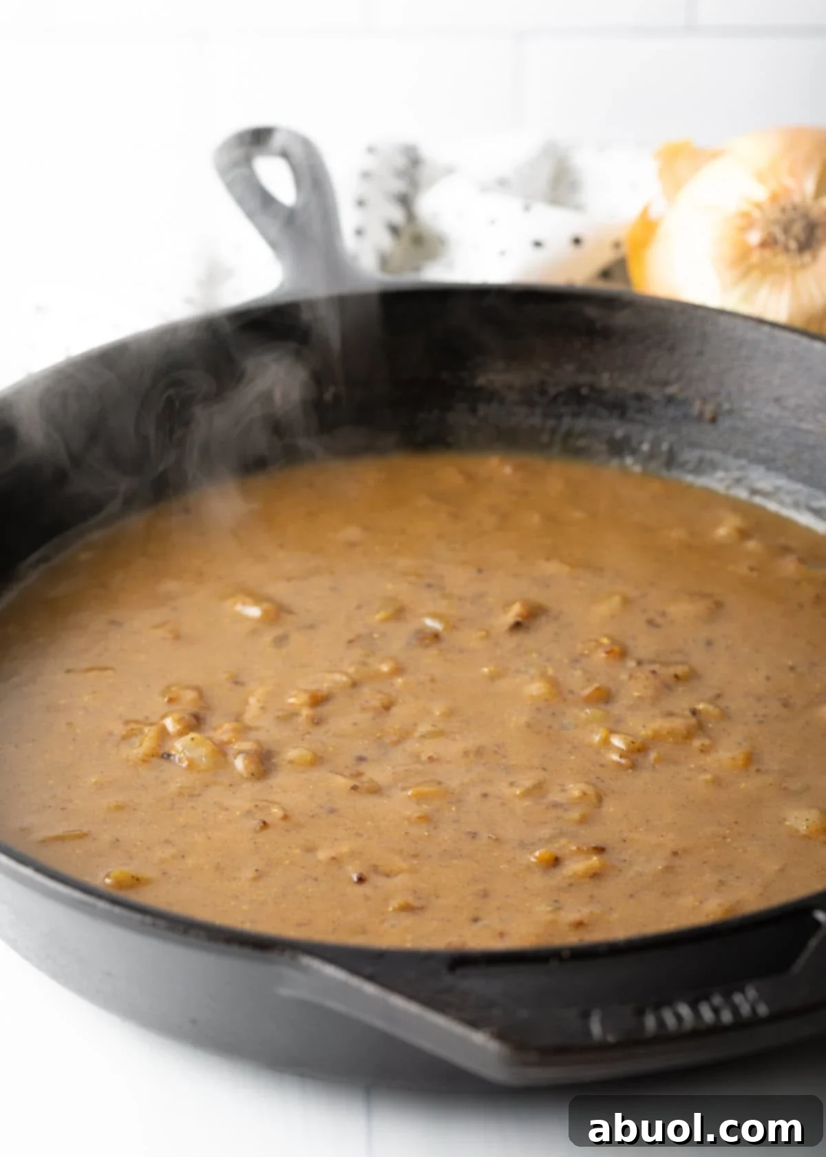 Rich, brown gravy simmering and thickening in a cast iron skillet, forming the essential base for the smothered chicken dish.