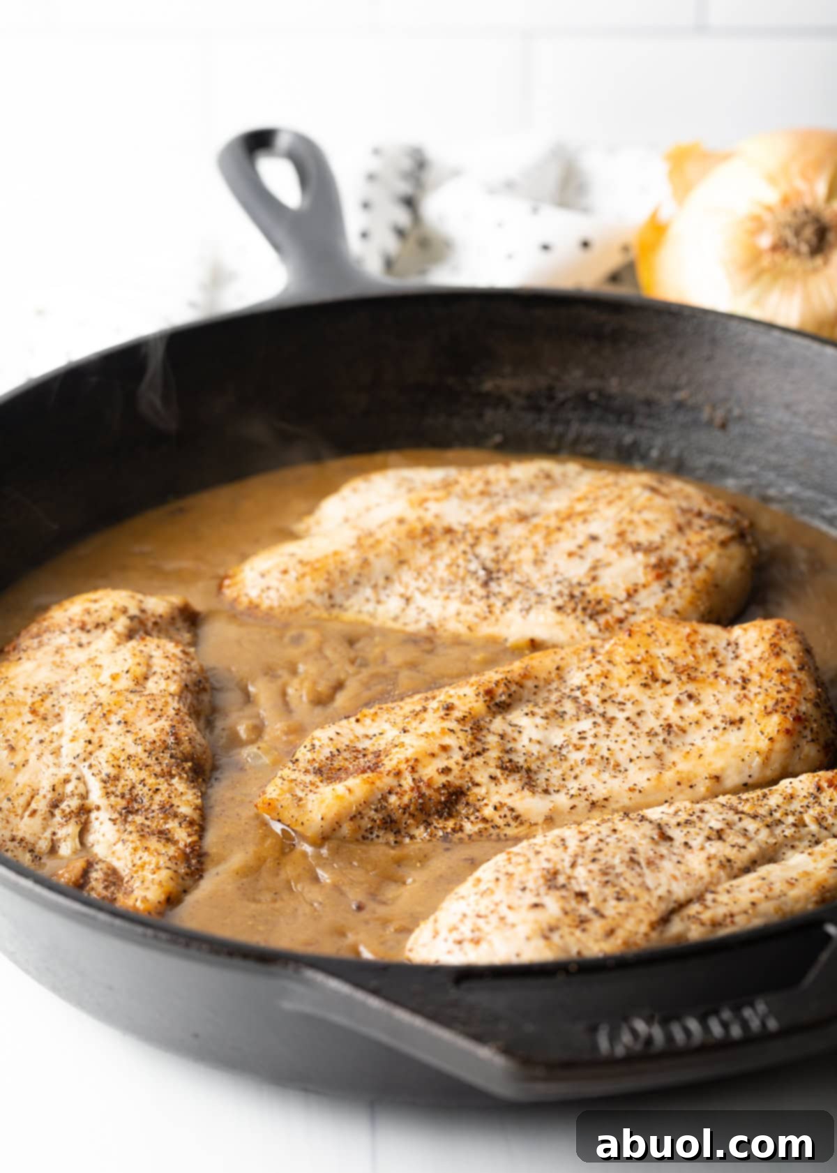 Tender chicken breasts immersed in a rich, brown gravy within a heavy cast iron skillet, ready for the final toppings.