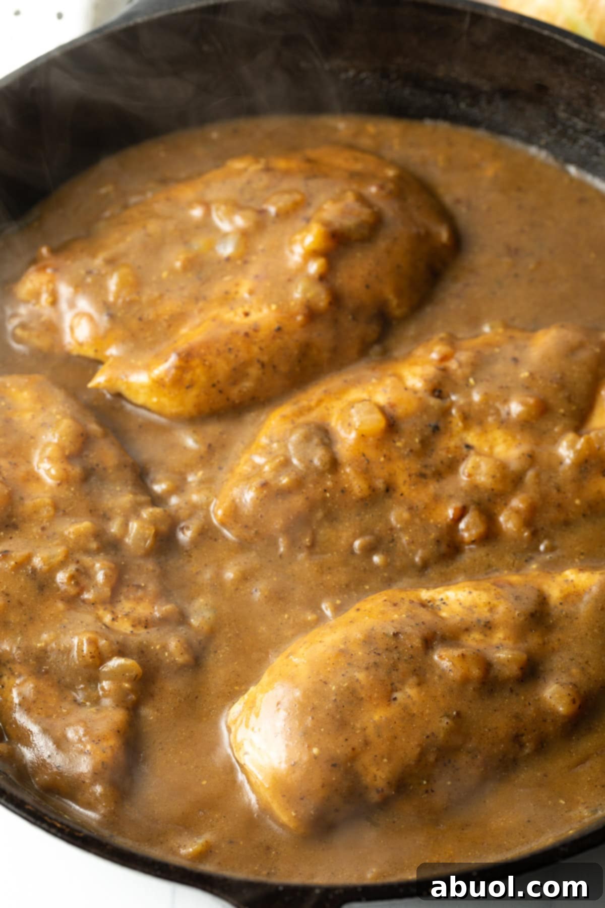 Overhead view of juicy boneless, skinless chicken breasts completely smothered in a rich, golden-brown gravy within a cast iron skillet, showcasing the inviting texture.