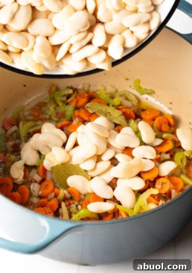 Adding soaked lima beans to the pot with the vegetable trinity