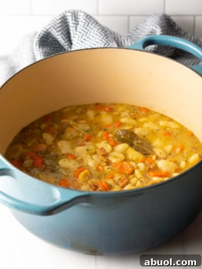 Large pot with chicken stock, carrots, beans, bacon, bay leaf, and seasonings simmering