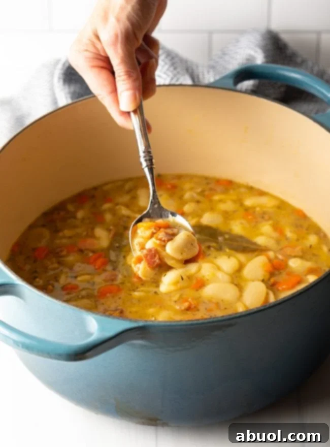 Hand spooning butter beans with bacon from a large pot