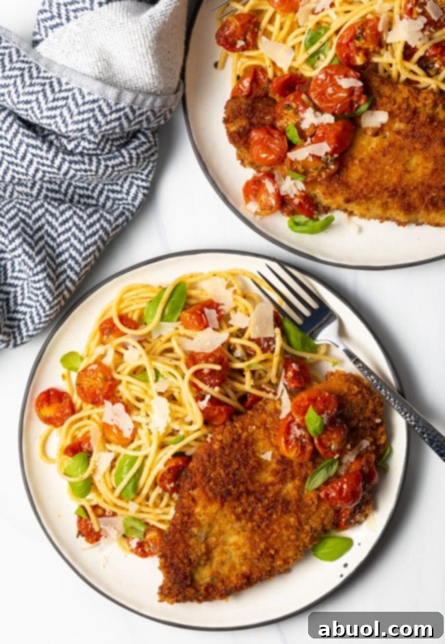overhead view two plates of pasta with fried chicken breasts and cherry tomato sauce