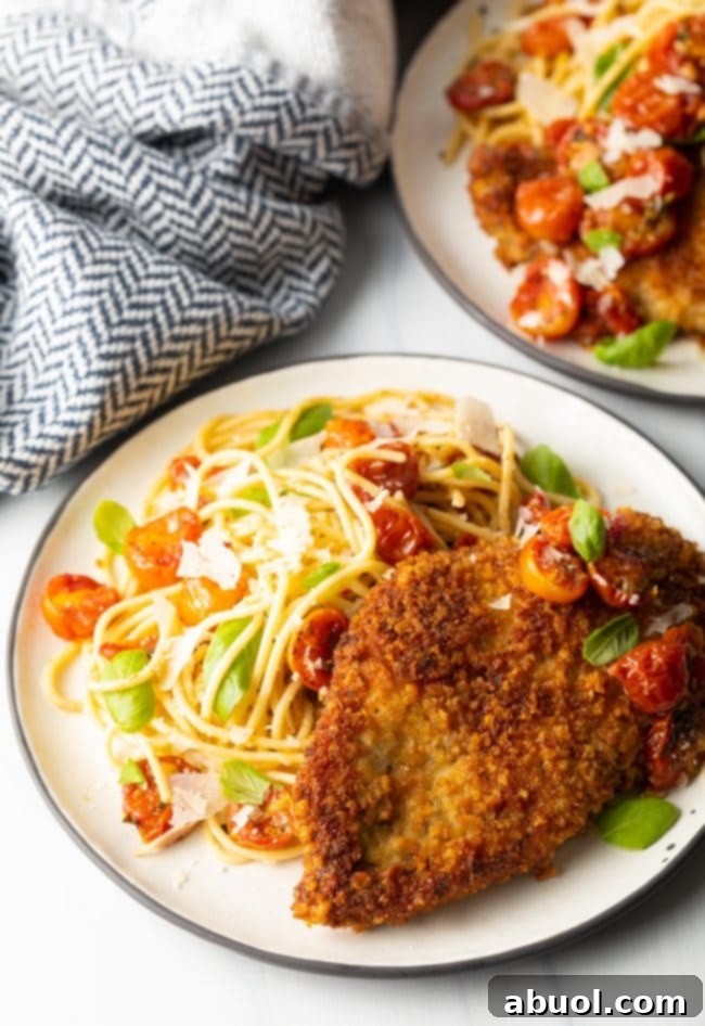 finished plate of pan fried or oven baked crispy Italian chicken cutlets with pasta and cherry tomato sauce on the side
