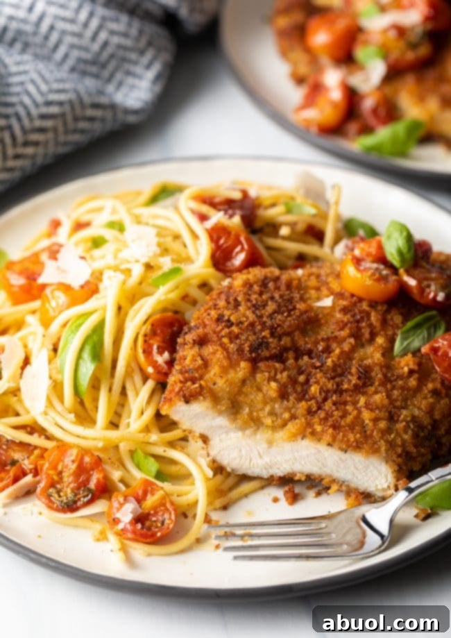 final shot showing Italian chicken cutlet cut into with a fork on a plate, spaghetti and cherry tomato sauce on the side