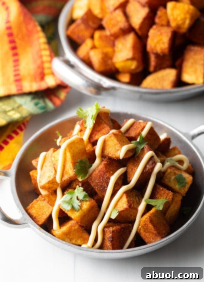 bowl of crunchy patatas bravas in a silver bowl with aioli and cilantro on top
