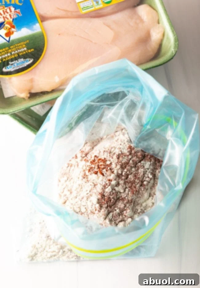 plastic zipper bag filled with seasonings and flour next to a package of raw chicken breasts