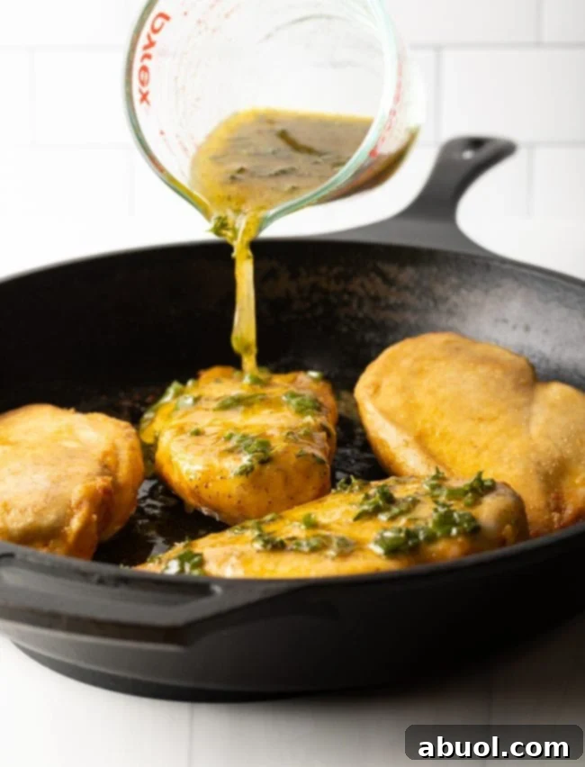 cast iron skillet with golden chicken breasts ready to go in the oven, lemon garlic sauce being poured on top from a glass measuring cup