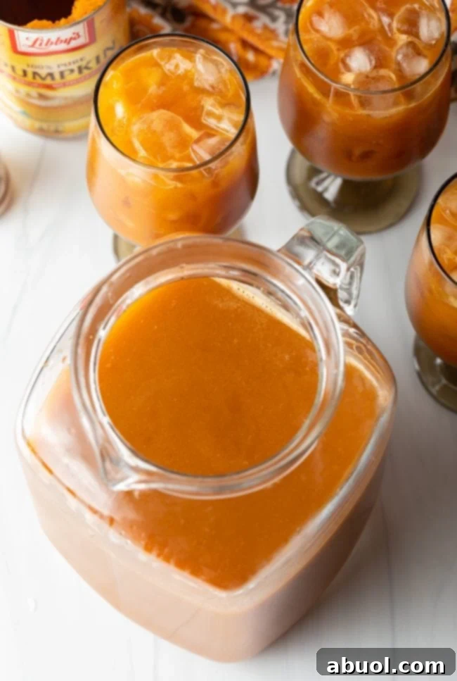 Overhead view of a glass filled with vibrant pureed pumpkin juice, with other glasses of iced juice blurred in the background, showcasing the fresh blend.