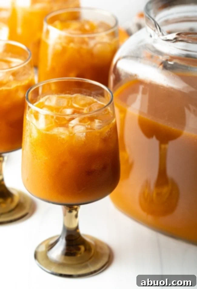 A glass of iced pumpkin juice with fruit over ice, positioned next to a pitcher brimming with the vibrant orange juice, ready for serving.