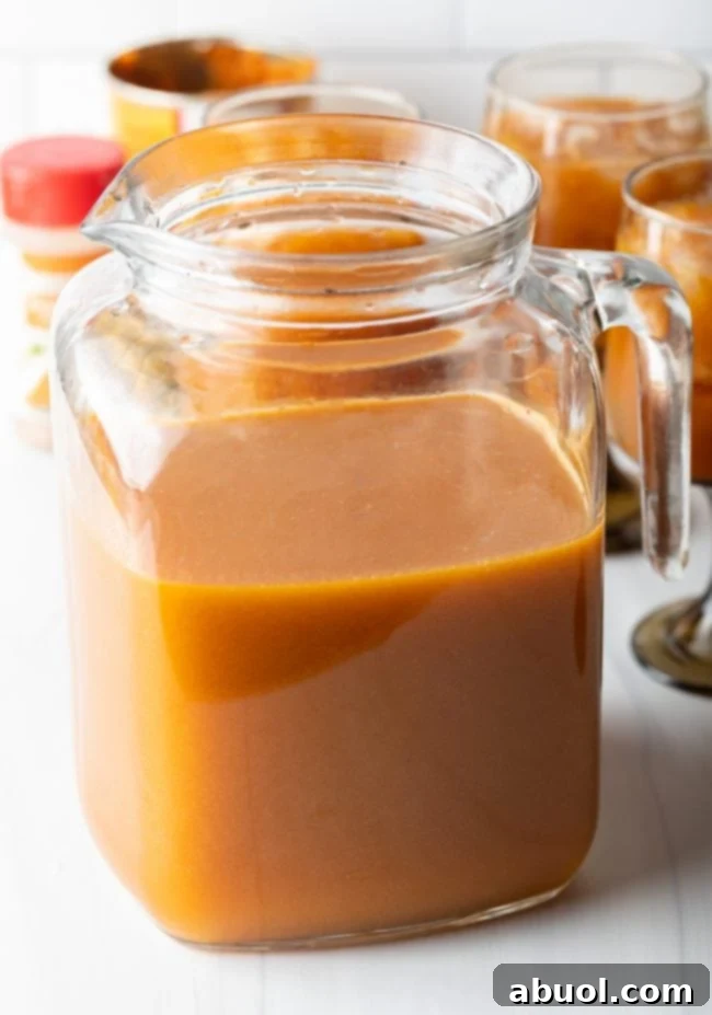 A elegant glass pitcher, half-filled with the rich, orange liquid of freshly blended Harry Potter Pumpkin Juice, ready for chilling or serving.