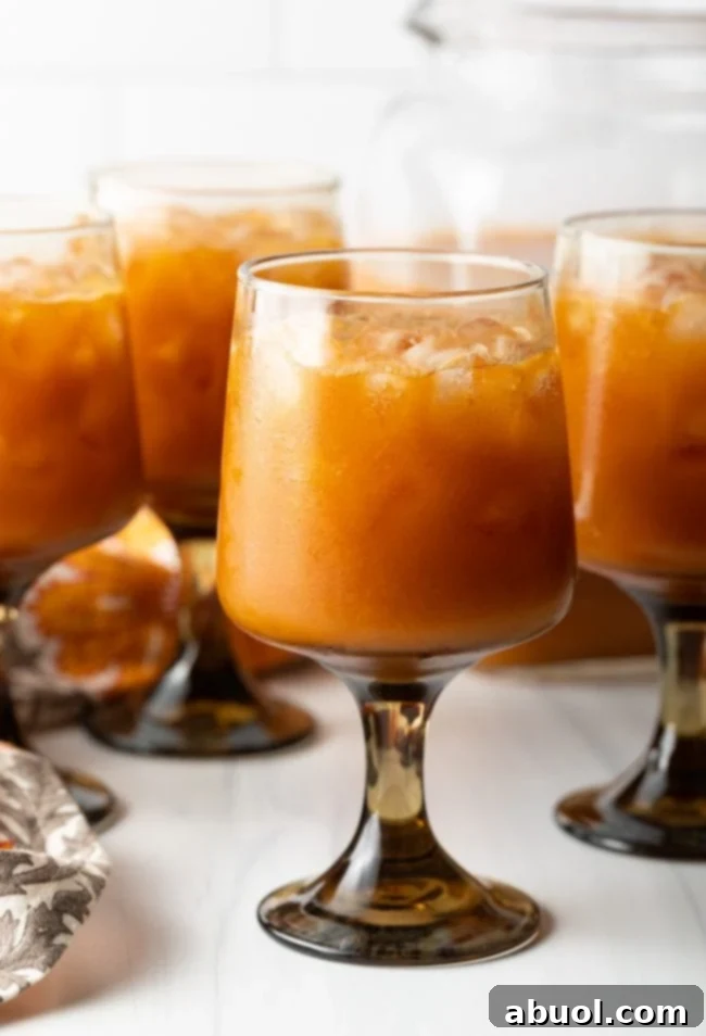 A side view of classic goblets brimming with iced, orange Harry Potter Pumpkin Juice, set against a warm, inviting backdrop.