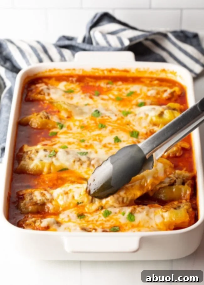 Metal tongs grabbing a sausage stuffed banana pepper from a baking dish, showcasing the melted cheese and marinara