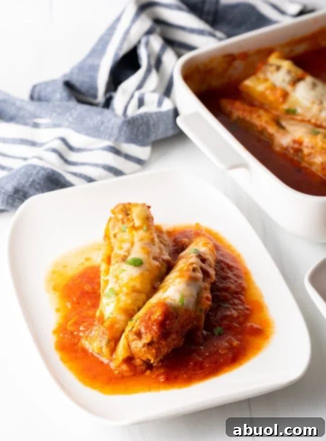Two generously stuffed banana peppers on a plate, covered in marinara and melted cheese