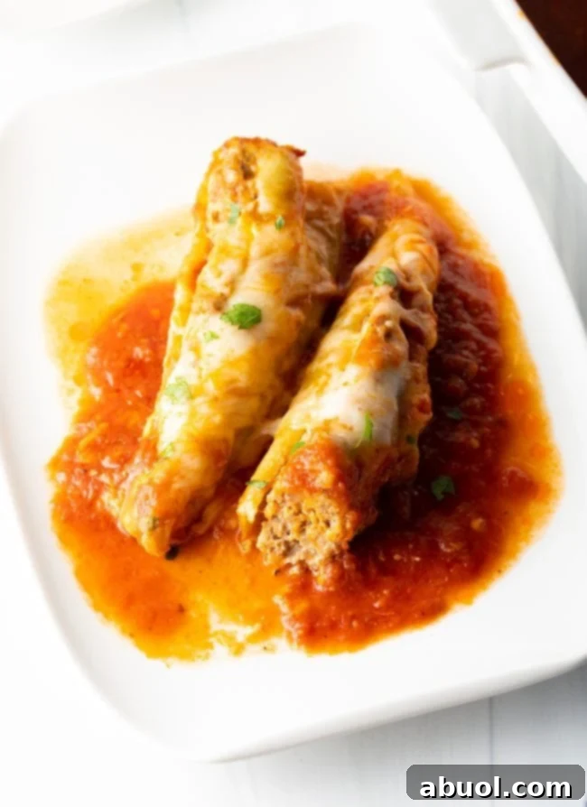 Two baked sausage stuffed banana peppers with melted cheese on a plate with marinara sauce