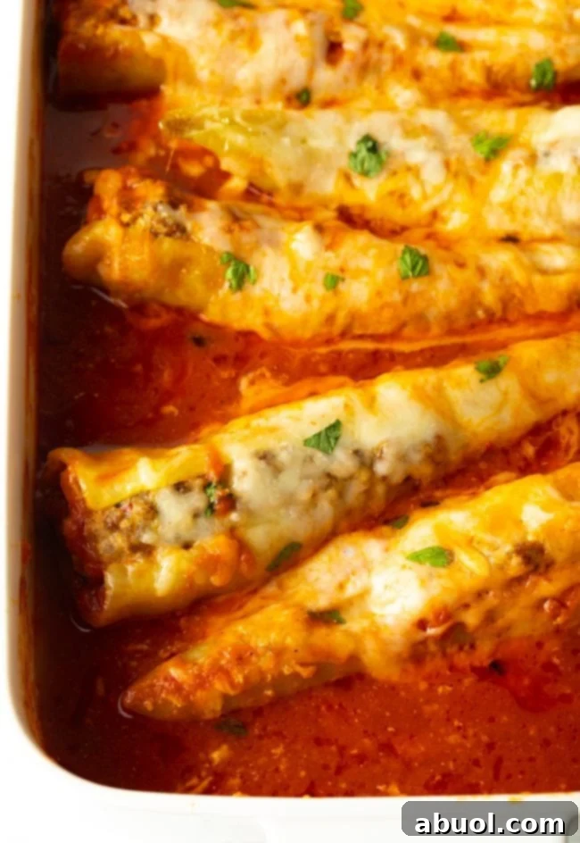 Top view of baked sausage stuffed banana peppers swimming in marinara sauce in a baking dish, covered with melted cheese and fresh parsley