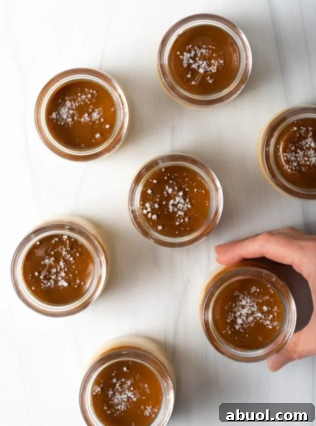 Close-up top view of jars filled with creamy butterscotch budino, generously topped with glistening salted caramel and a sprinkle of sea salt