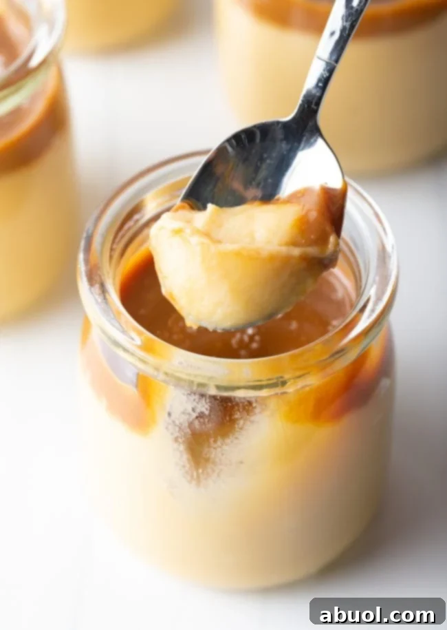 A spoon scooping a generous portion of thick, creamy butterscotch budino from a glass jar, revealing the layers of pudding and caramel