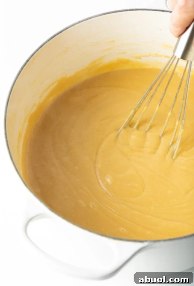 A close-up of a whisk continuously stirring the butterscotch budino mixture in a saucepan as it thickens to a creamy, smooth consistency