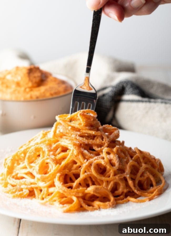 Fork swirling around some noodles coated in roasted red pepper sauce. 