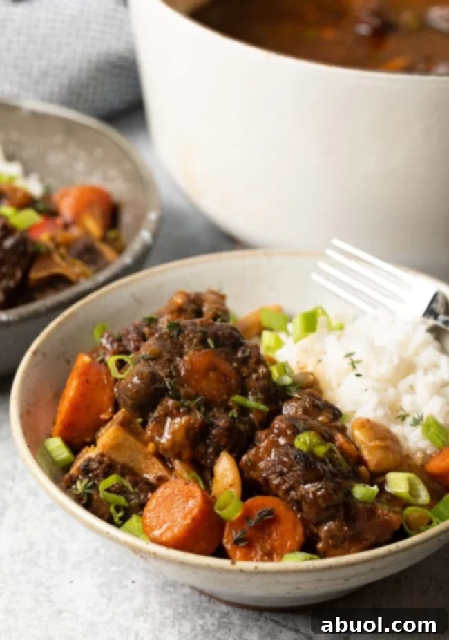 side view bowl Jamaican oxtail stew and white rice with other bowl in the background - Crockpot recipe