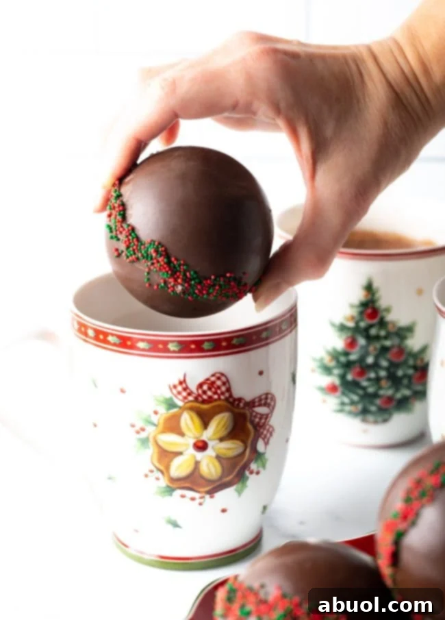 Velvet Cocoa Spheres 7 Hand holding hot chocolate ball over a Christmas mug.