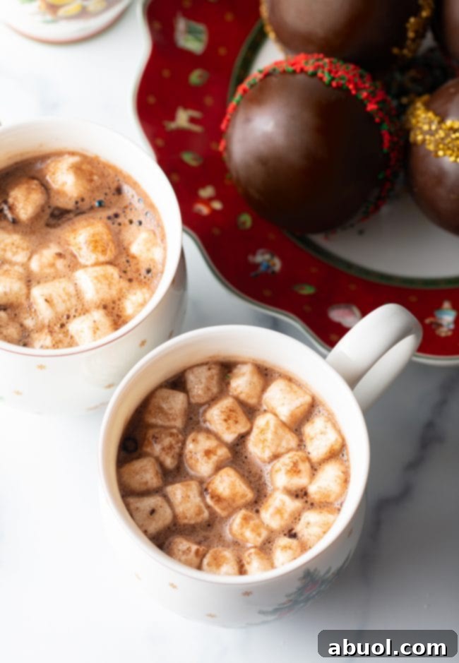 Velvet Cocoa Spheres 8 Two mugs of hot cocoa in Christmas mugs with plate of chocolate balls on festive plate in the background.