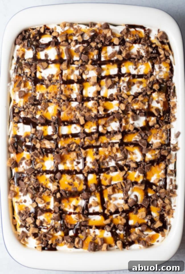 Top view of a finished Better Than Sex Chocolate Poke Cake in a large white baking dish, artfully drizzled with chocolate and caramel sauce and garnished with chopped toffee candy bars