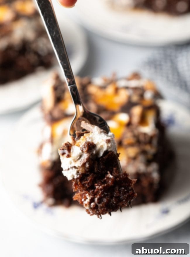 Forkful of chocolate cake with layers of caramel, whipped topping, and toffee candy bits