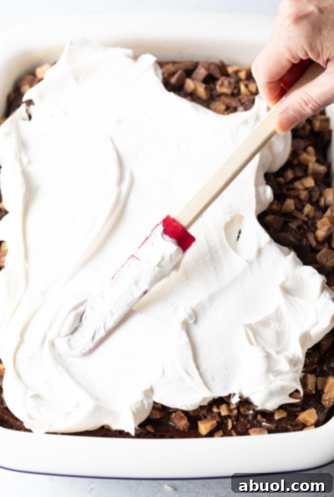 Adding a smooth, even layer of whipped topping on top of the chopped candy bars on the cake